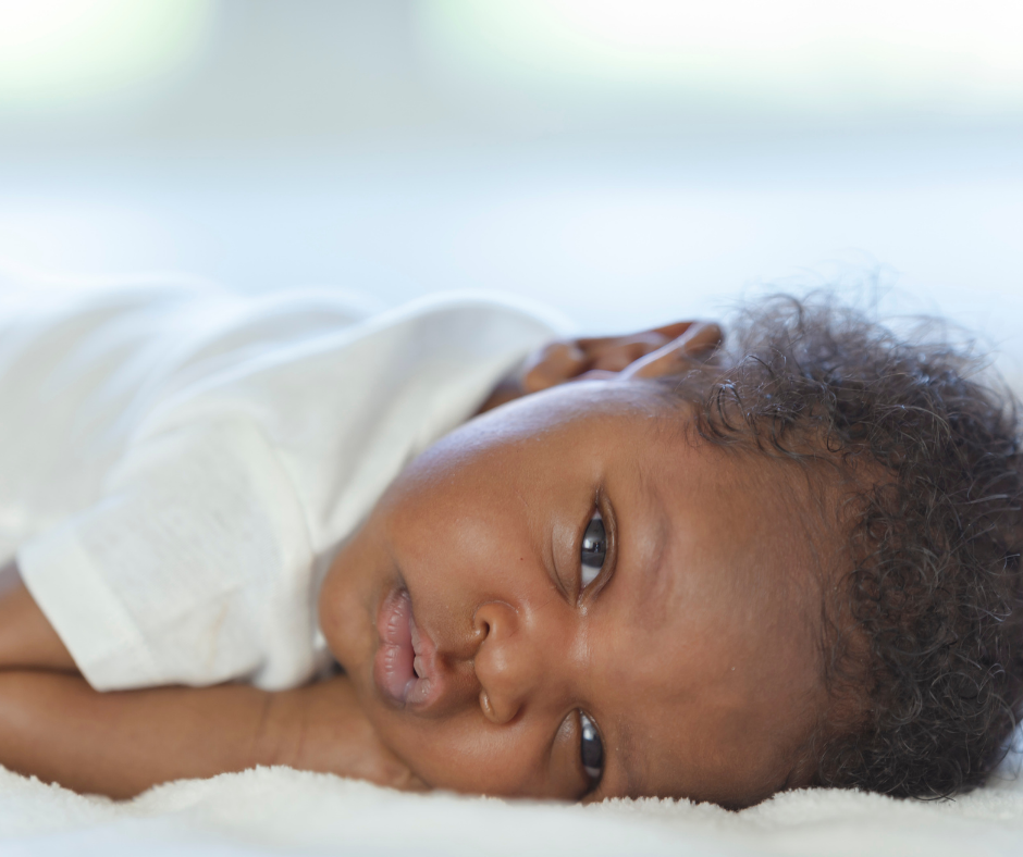 an image of a black baby with their eyes wide open on a white blanket. the background is blurred. the blog topic is on debunking sleep regression myths. 
